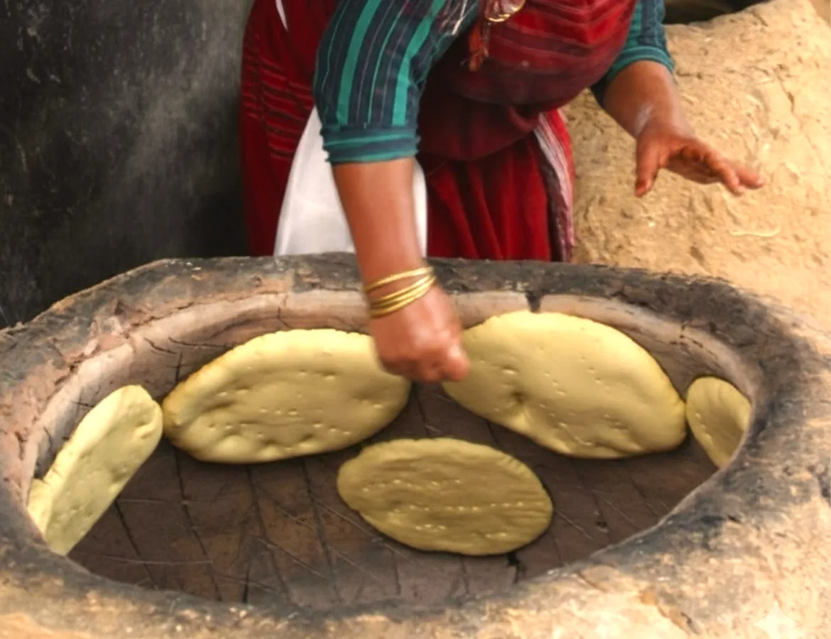 A woman baking tabouna flatbread in a traditional clay oven