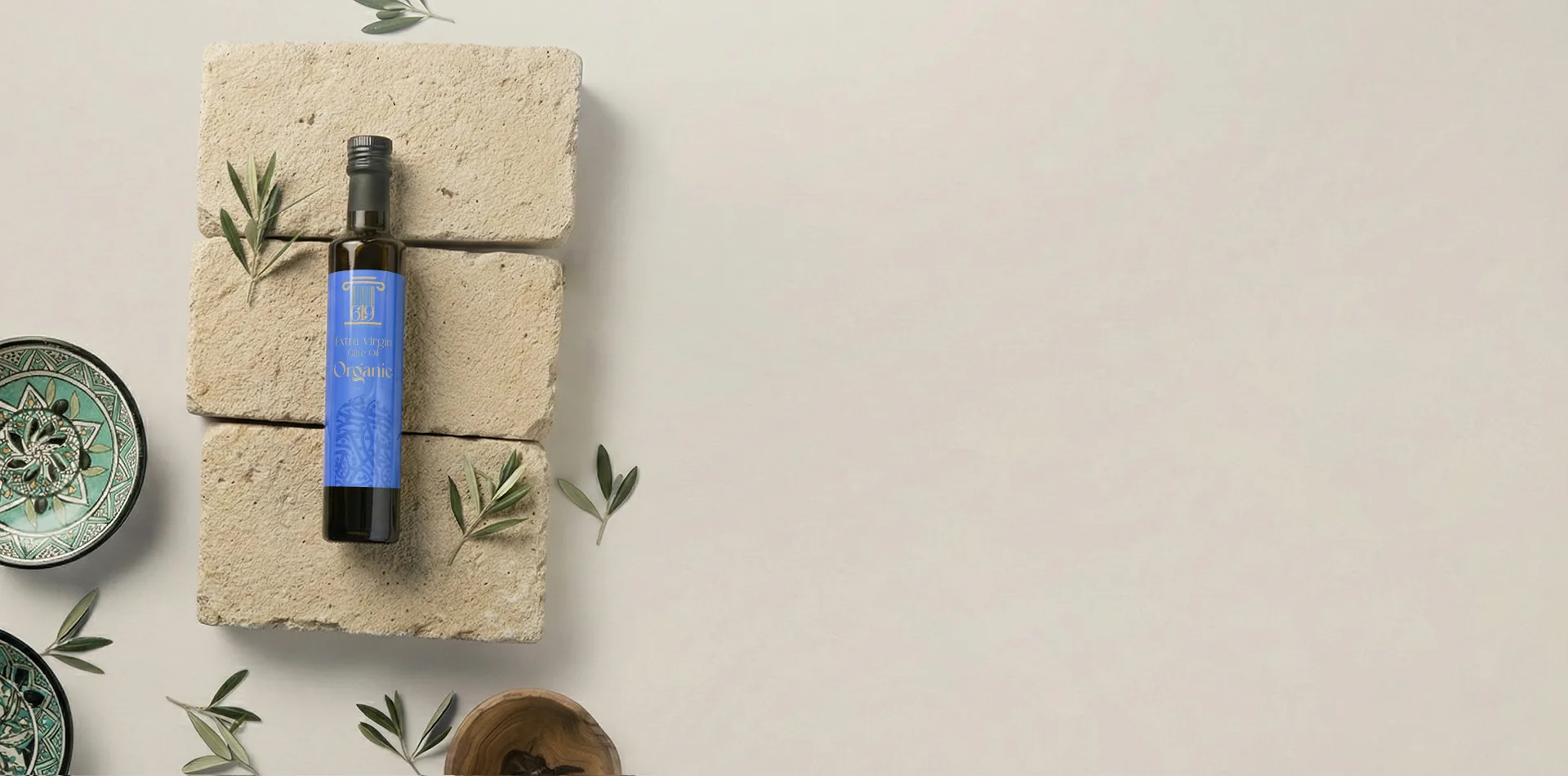 A bottle of 619 Organic Extra Virgin Olive Oil lying on limestone blocks among olive branches and Tunisian ceramics